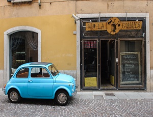En liten lyseblå bil står parkert foran en restaurant med et skilt som sier La Famiglia.