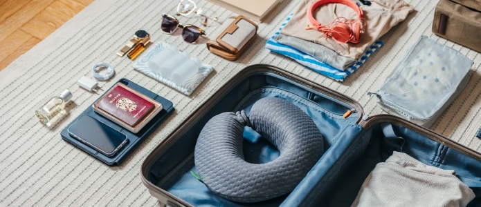 Åpen koffert på gulvet klar for en tur bort med pass, mobiltelefon, nettbrett, parfyme, solbriller, lommebok, hodetelefoner, lader, klær og en reisepute