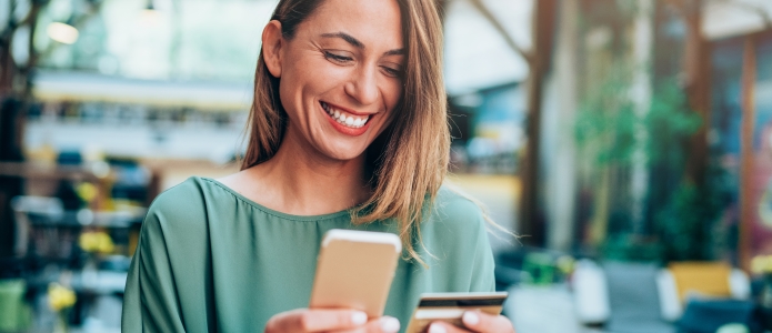Smilende kvinne ser på mobilen sin og sitt betalingskort