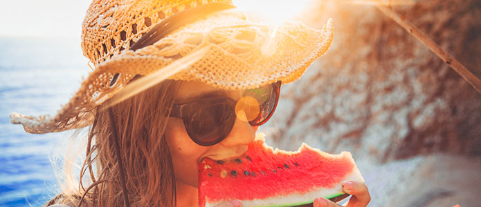 Jente med solhatt spiser et stykke vannmelon i solen